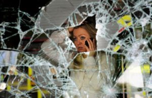 woman on phone staring out smashed window